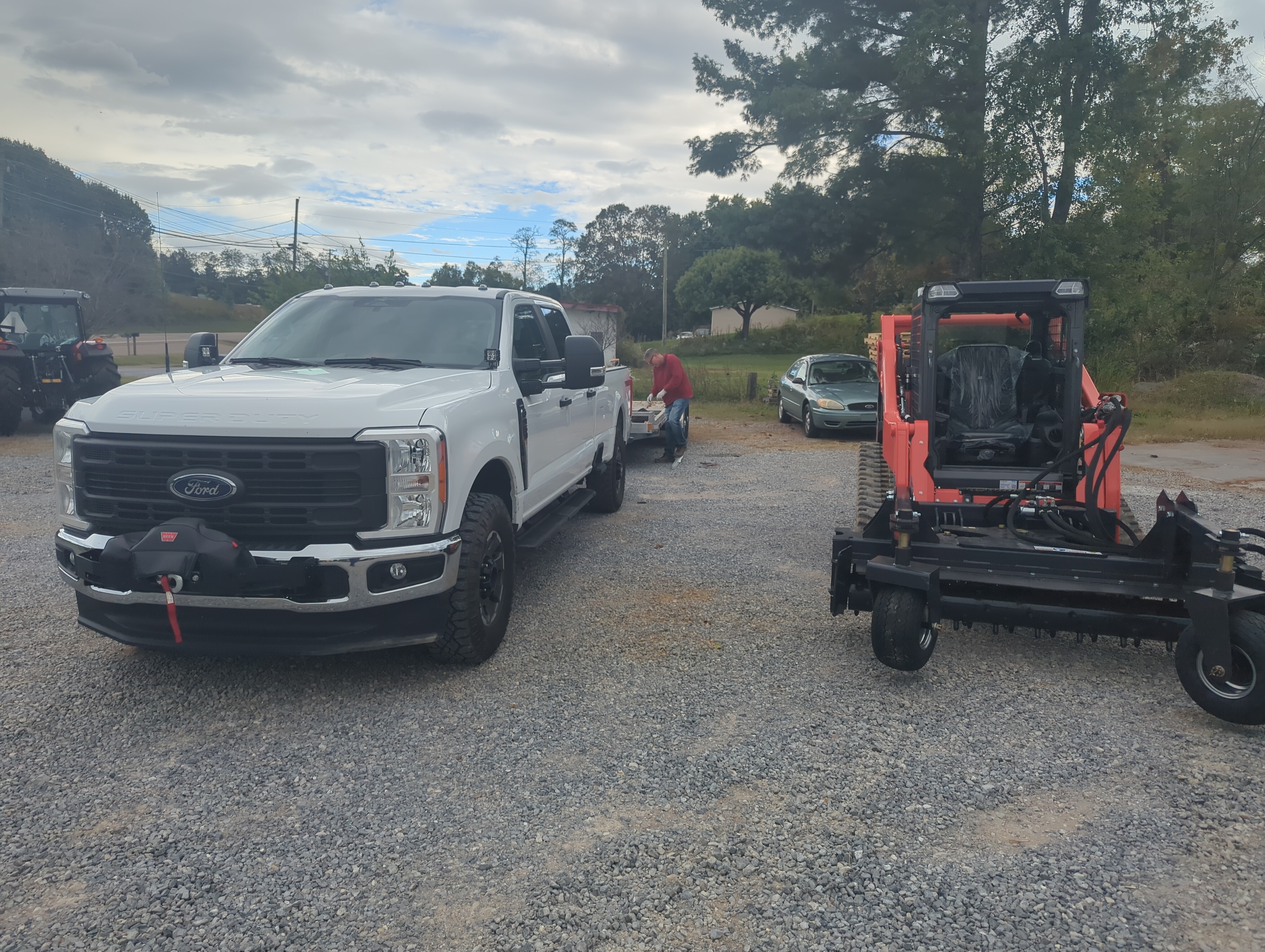 White Ford truck parked next to a red compact tractor on gravel lot