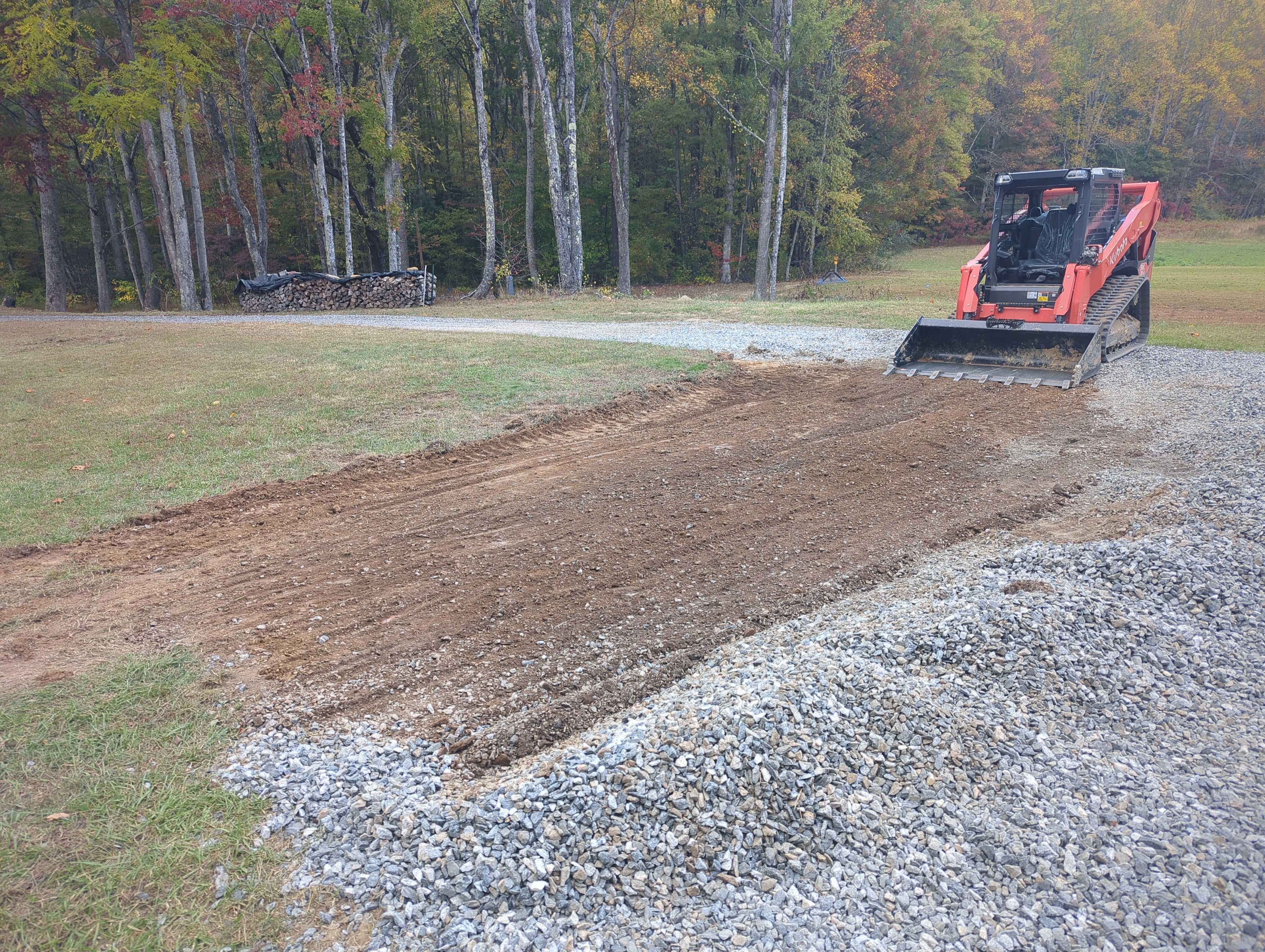 Red skid steer preparing ground with gravel and dirt in autumn forest