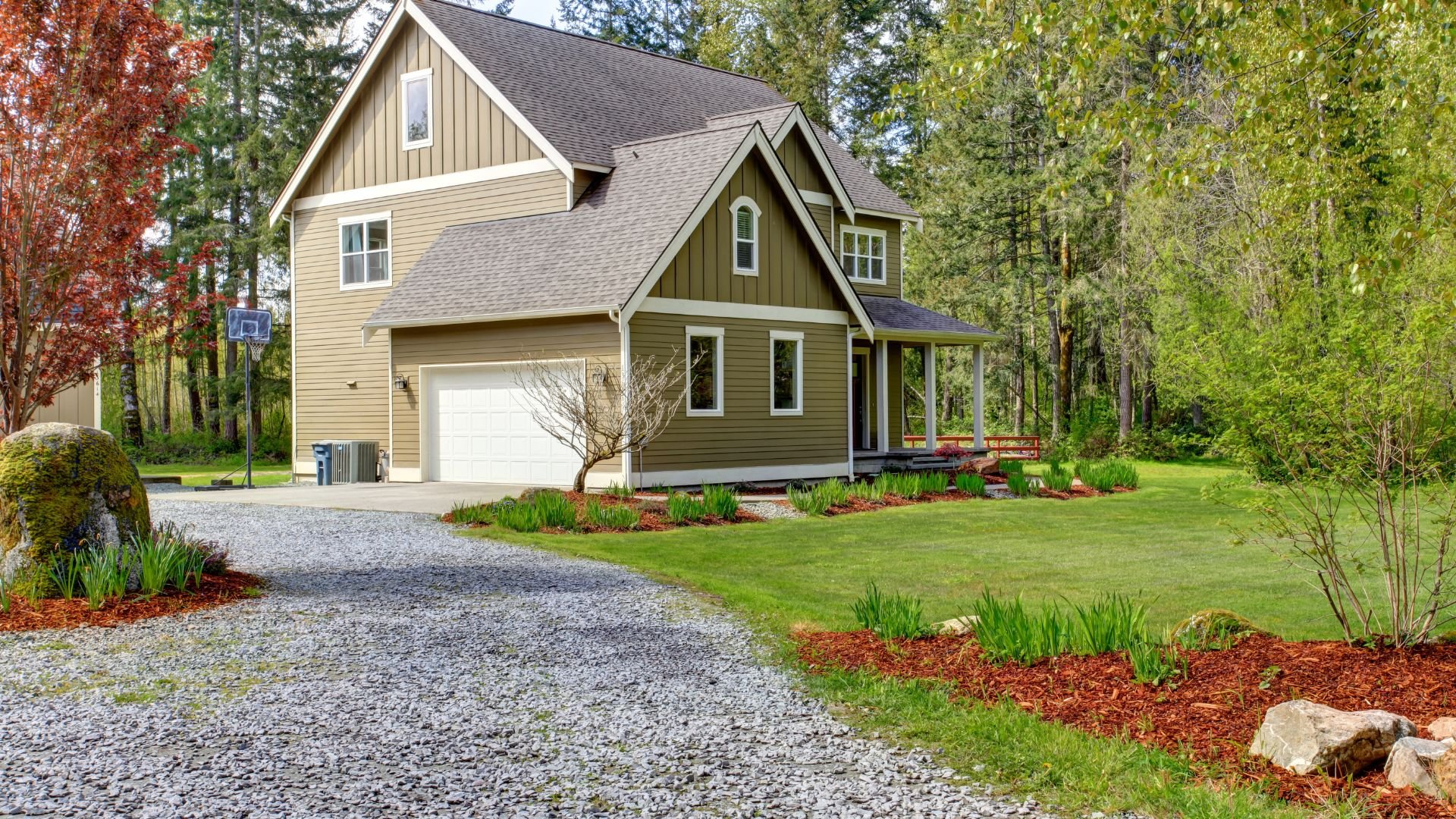 Two-story house with white garage in wooded area with landscaped yard