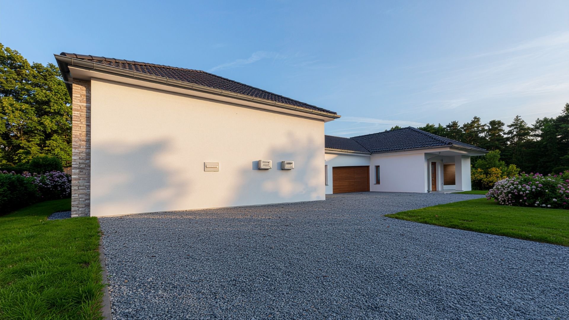 Modern white house with wooden garage, gravel driveway, and green landscaping