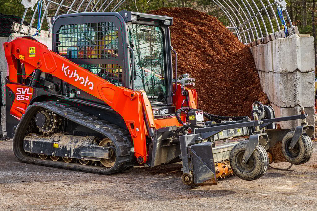 Red Kubota skid-steer loader with mulch pile in construction site