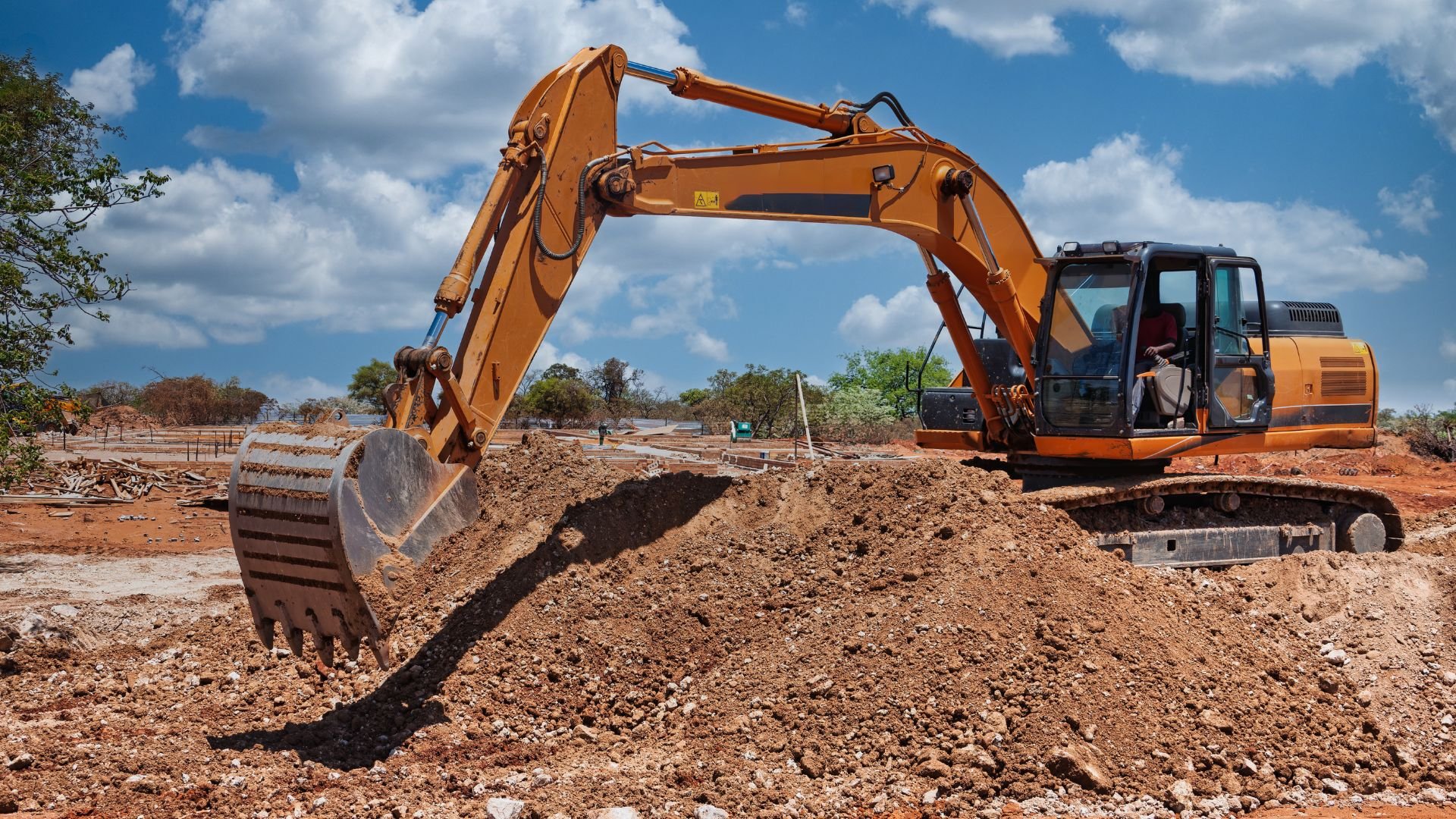 Yellow excavator digging soil at construction site under cloudy sky