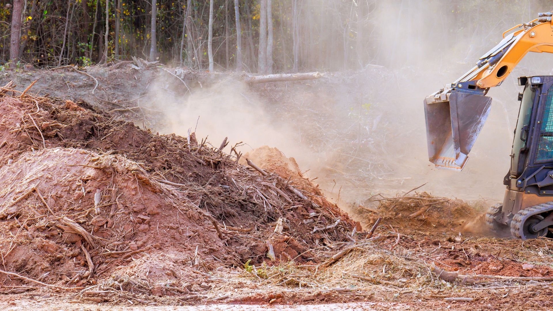 Excavator moving dirt and debris with dust clouds in forest clearing