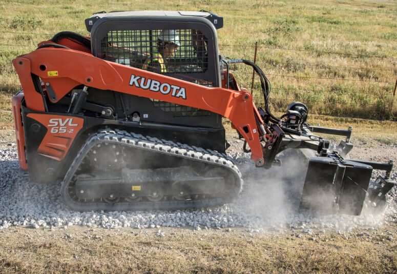 Red Kubota SVL skid-steer loader working on rocky terrain, kicking up dust